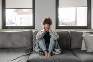A woman sits on a sofa looking unwell, emphasizing a sense of illness or fatigue indoors.
