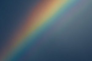 A vivid rainbow arches across a moody sky, creating a striking natural phenomenon.